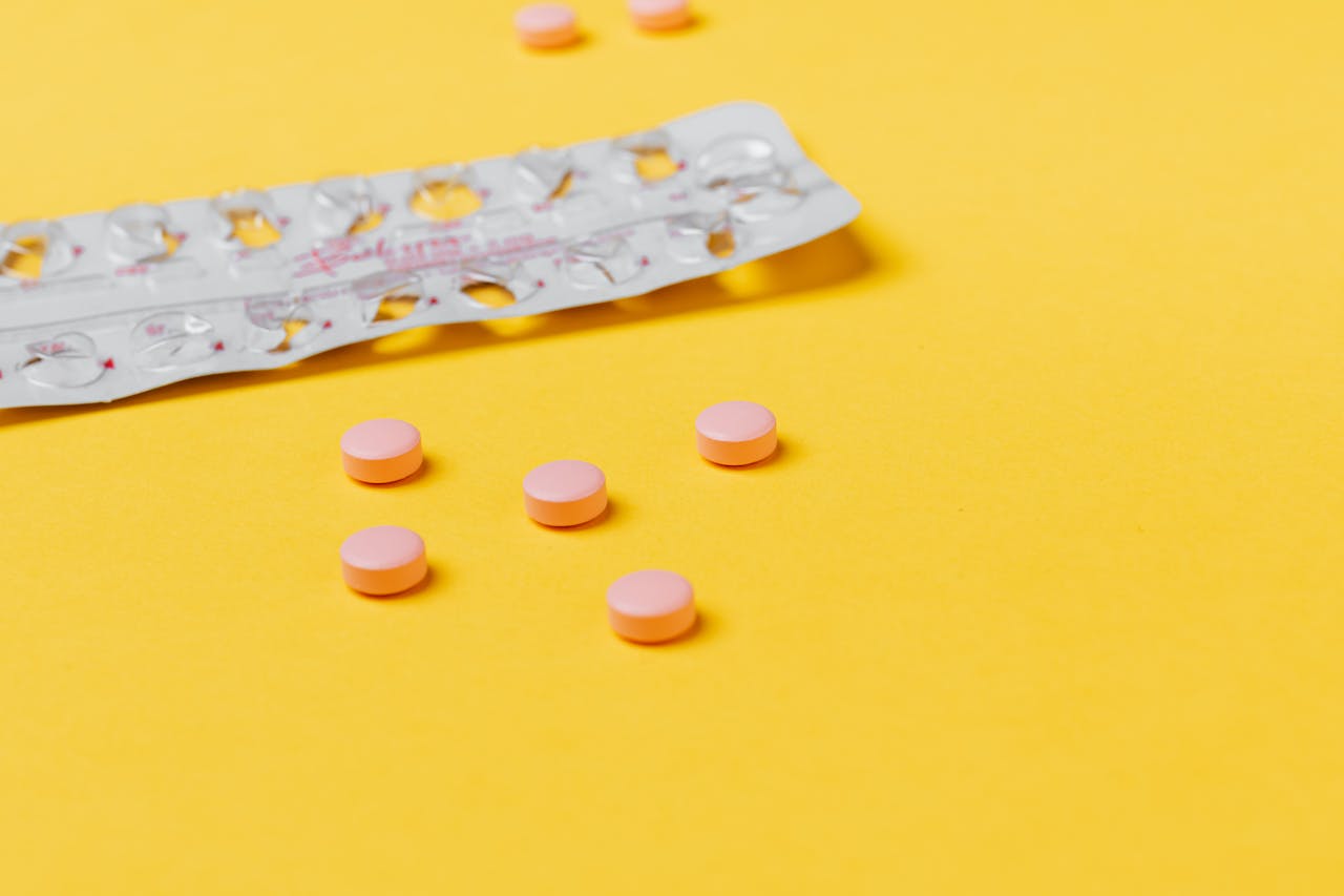 services-03 Pink pills scattered on a vibrant yellow background with an empty blister pack.