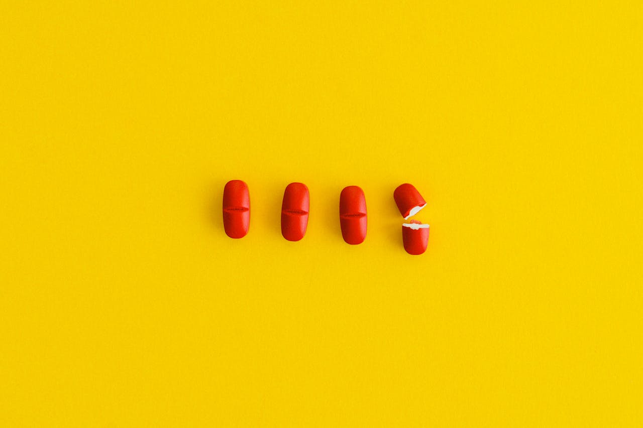 home-hero-2 Close-up of red capsules arranged on a bright yellow surface, symbolizing health and medication.